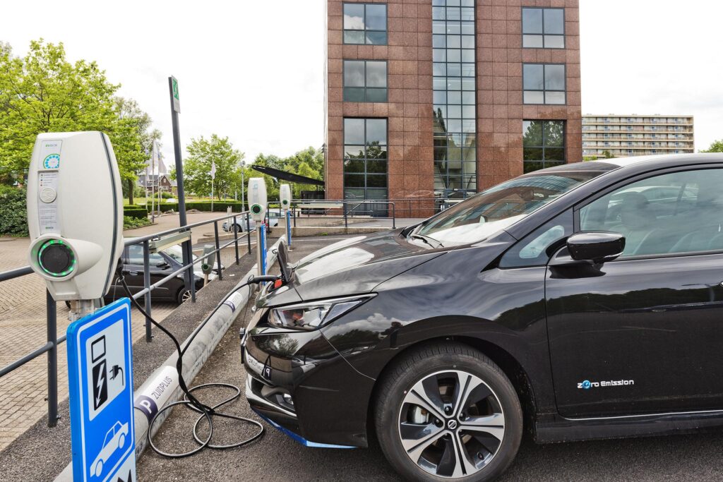 Electric car charging at a public charging station on Prof. W.H. Keesomlaan, with a modern office building in the background.